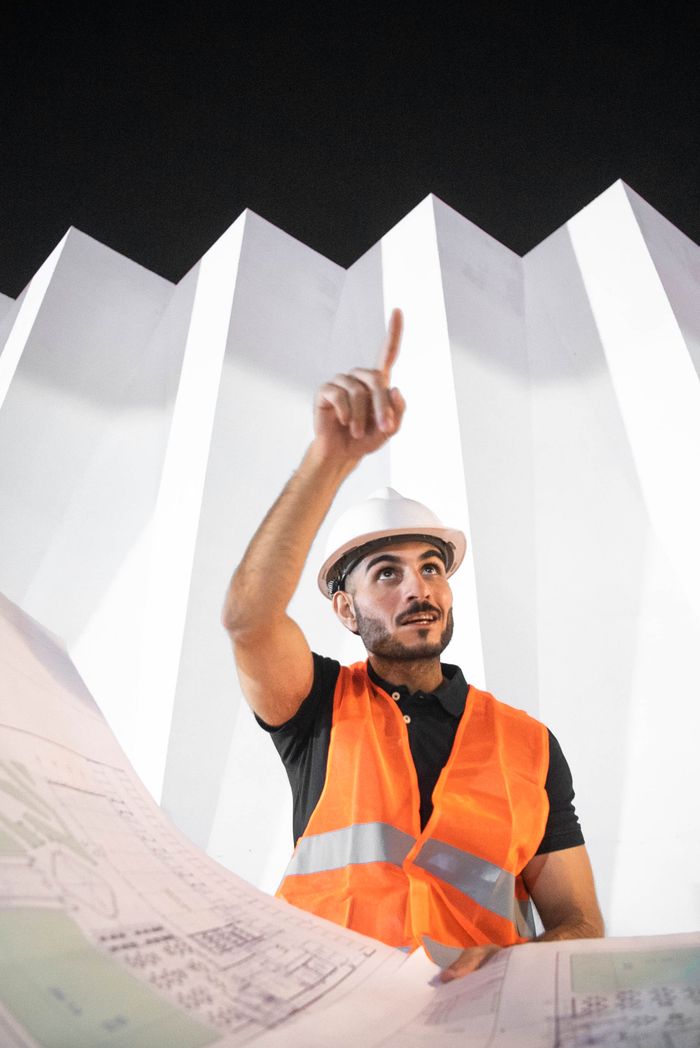 gallery-1 A construction worker in a helmet and vest analyzing blueprints under dramatic architecture.