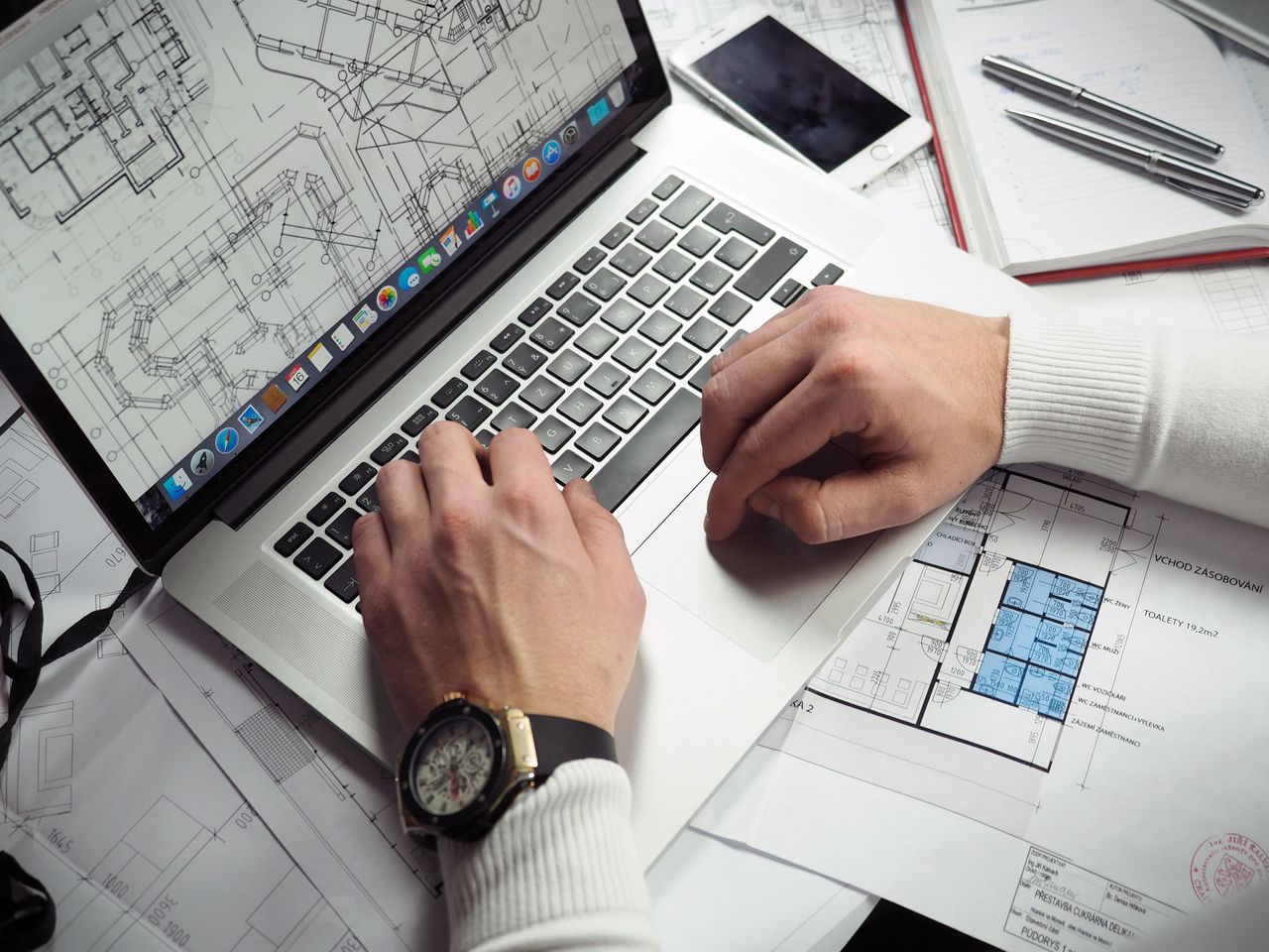 services-03 Architect reviewing detailed floor plans and schematics on a laptop with a smartphone nearby.