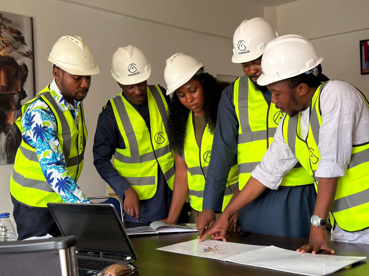 ours-journey Group of engineers in safety gear reviewing blueprints indoors.