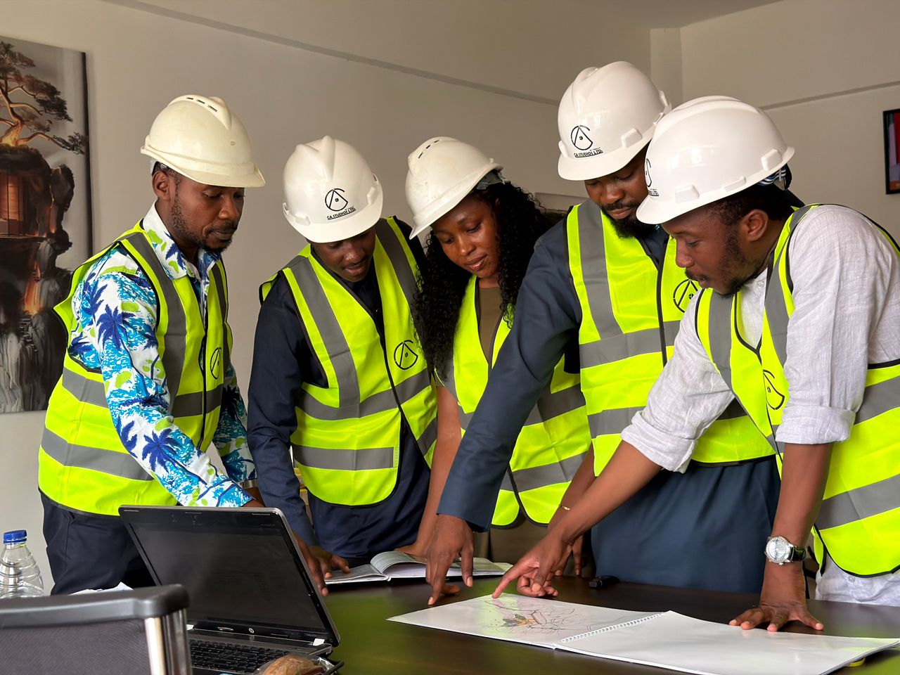 gallery-2 A diverse team of five engineers in safety gear examines construction plans indoors.