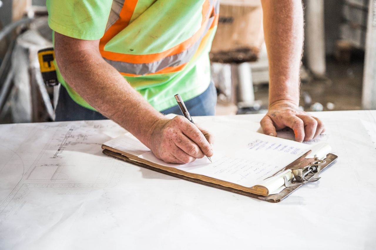 about-01 A construction worker writes notes on a clipboard at a construction site, emphasizing planning and precision.