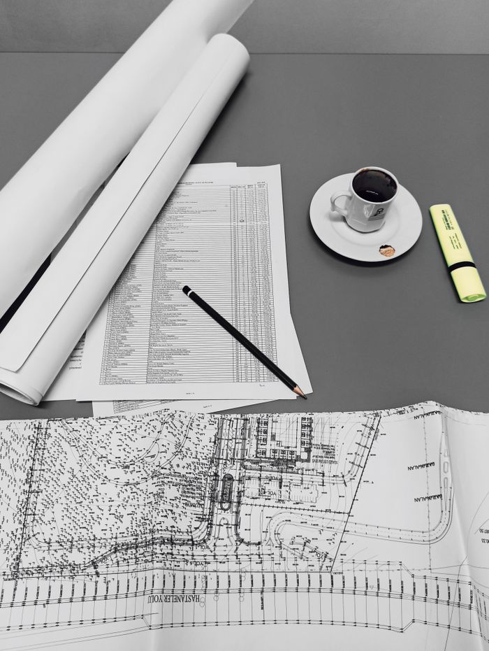 gallery-5 Architectural blueprints and drafts with a cup of coffee and stationery on a minimalist desk.