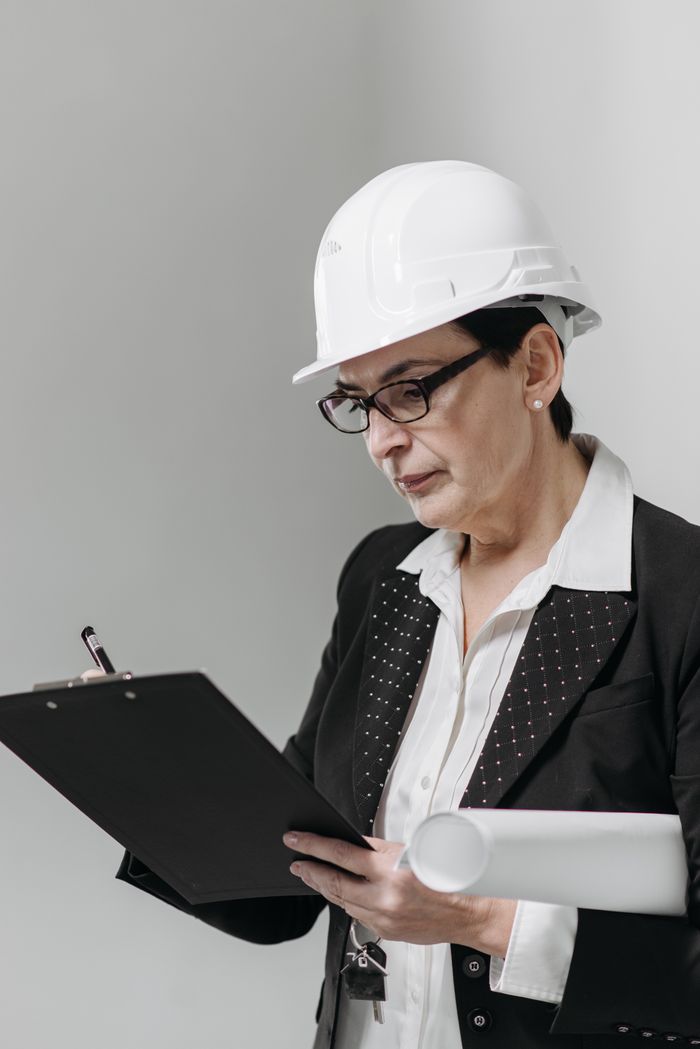 services-02 Middle-aged woman architect with eyeglasses and hard hat reviews construction plans indoors.