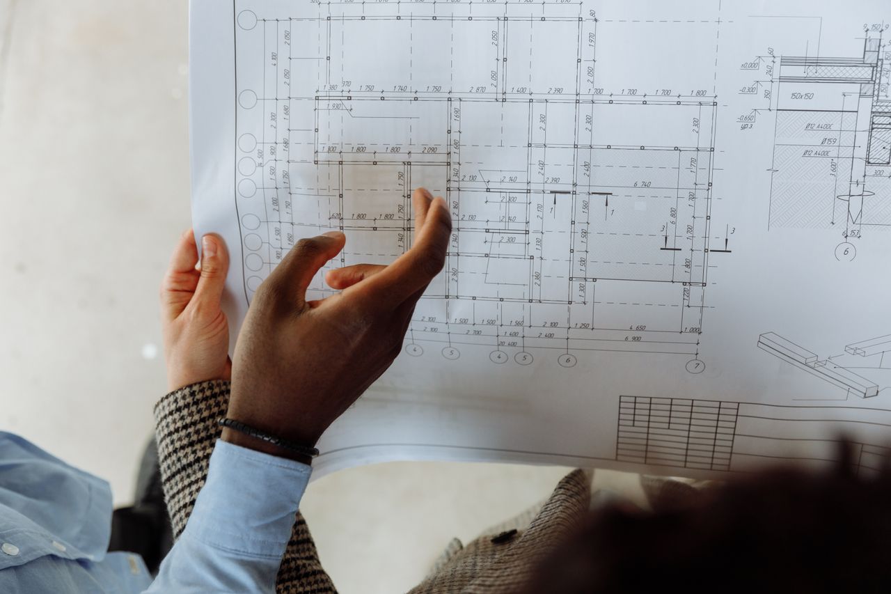 gallery-4 In-depth view of hands examining a detailed architectural blueprint with precise measurements.