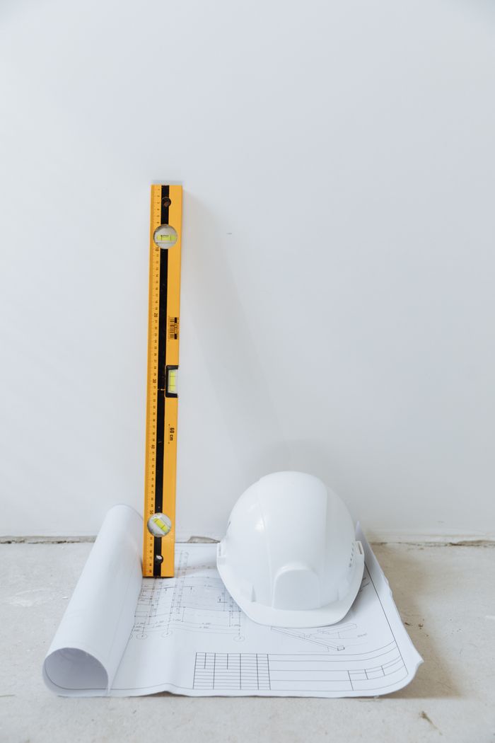 why-choose-us Rolled blueprint, hard hat, and level tool arranged against a white background.